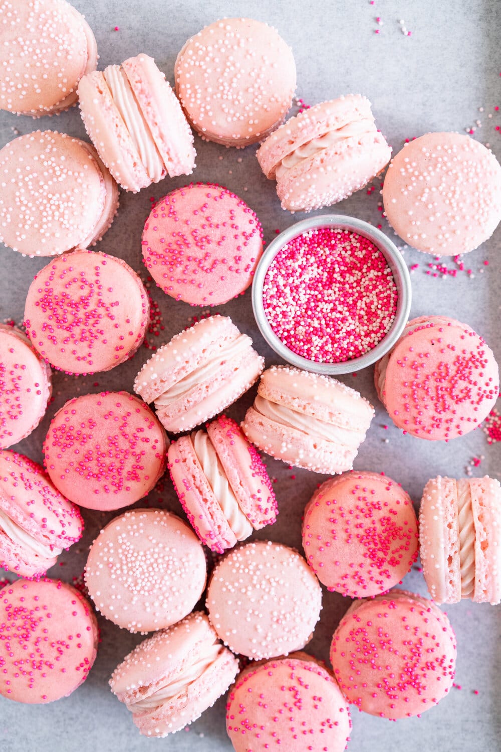 Pink macarons on paper with a dish of sprinkles