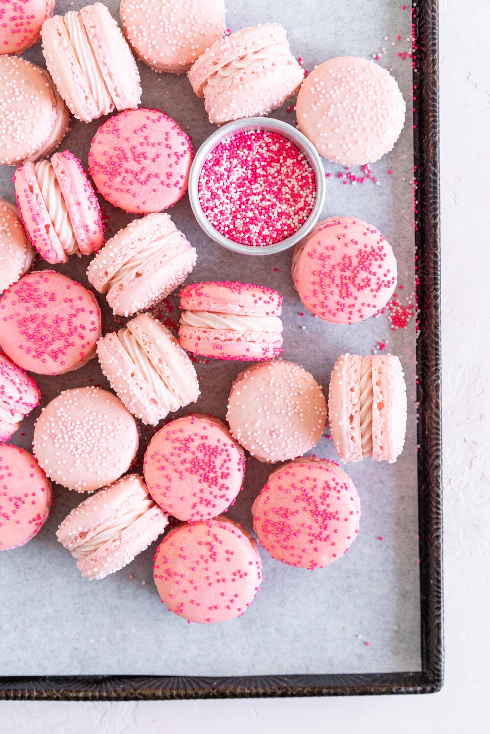pink macaron shells on a sheet pan with pink buttercream