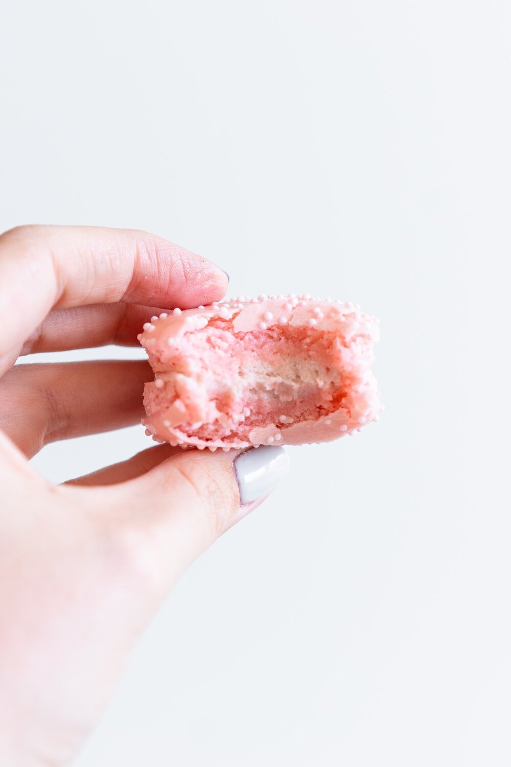 hand holding macaron with a bite taken out of it.