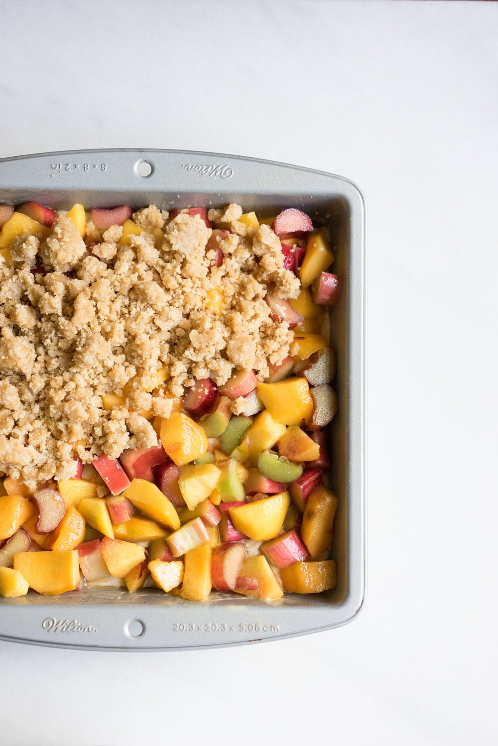 Peach and rhubarb crumb cake with brown butter streusel. This soft vanilla bean cake is covered with chopped fruit, and finished with a toasty, crunchy brown butter streusel.
