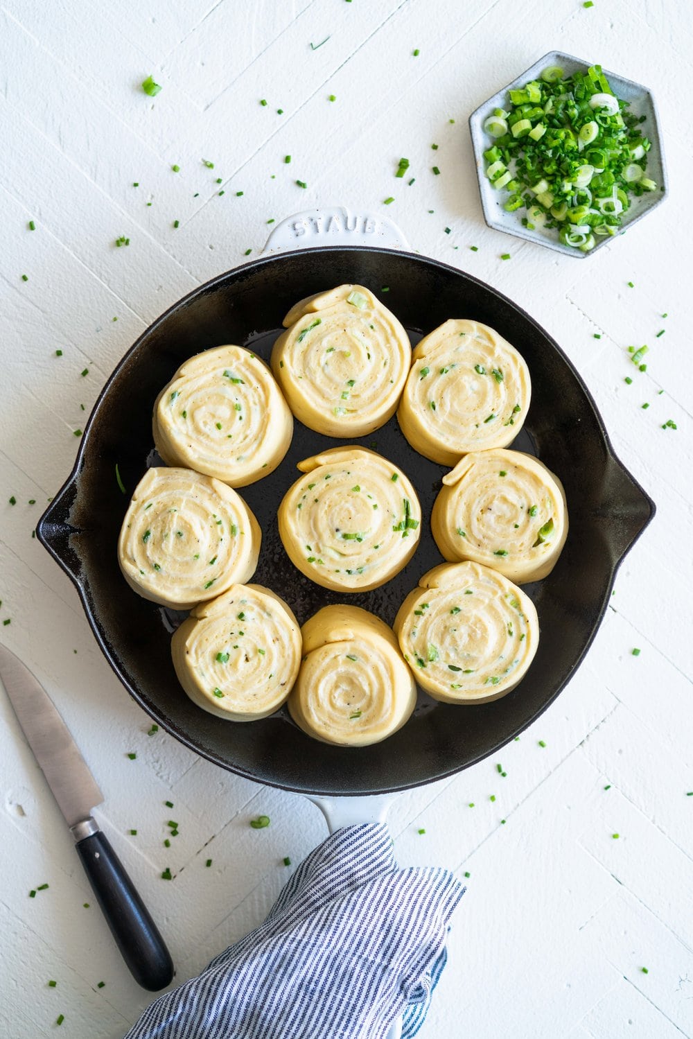 Cheese, Spring Onion, and Chive Brioche Buns - fluffy brioche is rolled out thin, then spread with a cheese sauce filling, sprinkled with spring onion and chives, and rolled up into a tight spiral. It is then cut up into buns, snuggled into a skillet, and baked to golden perfection. The perfect savoury bun! #cheesebuns #cheeserolls #cheeseandchive