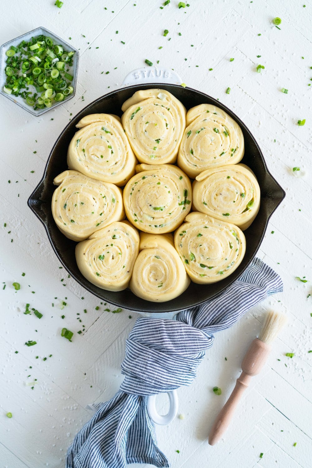 Cheese, Spring Onion, and Chive Brioche Buns - fluffy brioche is rolled out thin, then spread with a cheese sauce filling, sprinkled with spring onion and chives, and rolled up into a tight spiral. It is then cut up into buns, snuggled into a skillet, and baked to golden perfection. The perfect savoury bun! #cheesebuns #cheeserolls #cheeseandchive