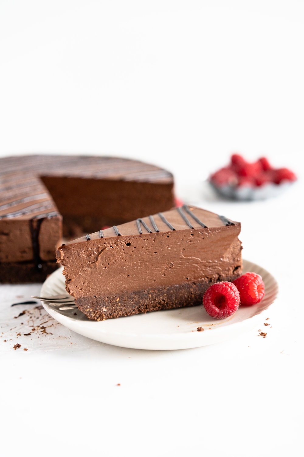 No Bake Chocolate Cheesecake - a chocolate graham cracker base is topped with a silky, no bake chocolate cheesecake filling, and finished with a drizzle of sweet, sticky raspberry balsamic glaze. This dessert comes together quickly, and is perfect for feeding a crowd. #cheesecake #chocolatecheesecake #nobakecheesecake