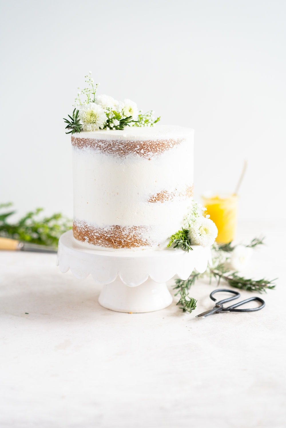 Olive Oil Layer Cake with Meyer Lemon Curd and Rosemary German Buttercream. Fruity olive oil cake is filled with a zesty meyer lemon curd, and finished in a semi naked style with a rosemary german buttercream and spring flowers. #nakedcake #oliveoilcake #meyerlemon