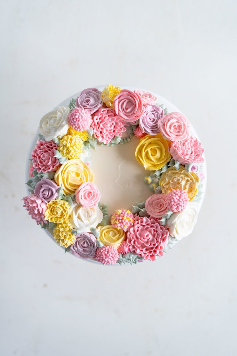 Lavender Blackberry Cake with Cream Cheese Frosting and a Piped Floral Wreath. Layers of delicately flavoured lavender cake are filled with a cream cheese frosting and blackberry jam, and topped with a beautiful floral wreath made from piped swiss meringue buttercream flowers. #pipedflowers #lavendercake #swissmeringuebuttercream #icingonthecakebook