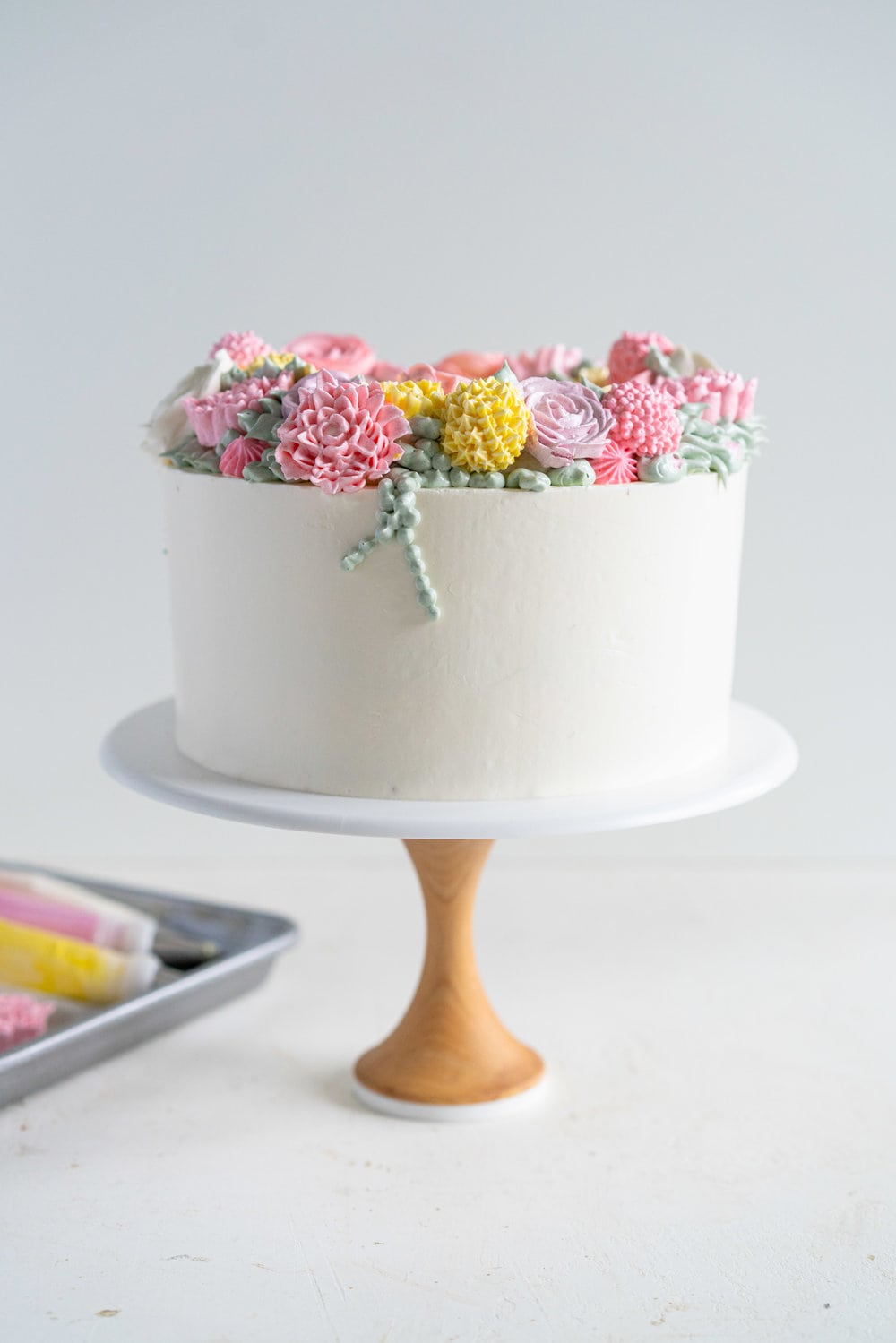 Lavender Blackberry Cake with Cream Cheese Frosting and a Piped Floral Wreath. Layers of delicately flavoured lavender cake are filled with a cream cheese frosting and blackberry jam, and topped with a beautiful floral wreath made from piped swiss meringue buttercream flowers. #pipedflowers #lavendercake #swissmeringuebuttercream #icingonthecakebook