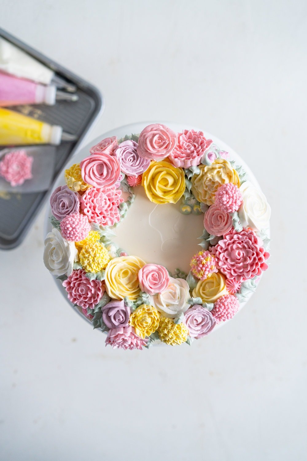 Lavender Blackberry Cake with Cream Cheese Frosting and a Piped Floral Wreath. Layers of delicately flavoured lavender cake are filled with a cream cheese frosting and blackberry jam, and topped with a beautiful floral wreath made from piped swiss meringue buttercream flowers. #pipedflowers #lavendercake #swissmeringuebuttercream #icingonthecakebook
