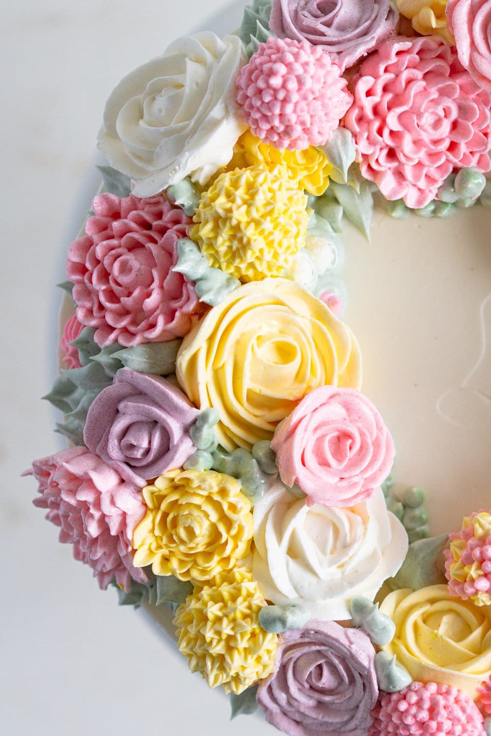 Lavender Blackberry Cake with Cream Cheese Frosting and a Piped Floral Wreath. Layers of delicately flavoured lavender cake are filled with a cream cheese frosting and blackberry jam, and topped with a beautiful floral wreath made from piped swiss meringue buttercream flowers. #pipedflowers #lavendercake #swissmeringuebuttercream #icingonthecakebook