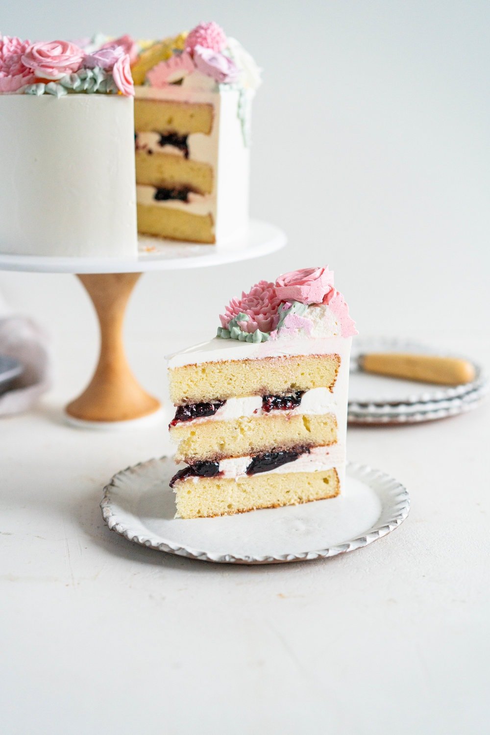Lavender Blackberry Cake with Cream Cheese Frosting and a Piped Floral Wreath. Layers of delicately flavoured lavender cake are filled with a cream cheese frosting and blackberry jam, and topped with a beautiful floral wreath made from piped swiss meringue buttercream flowers. #pipedflowers #lavendercake #swissmeringuebuttercream #icingonthecakebook