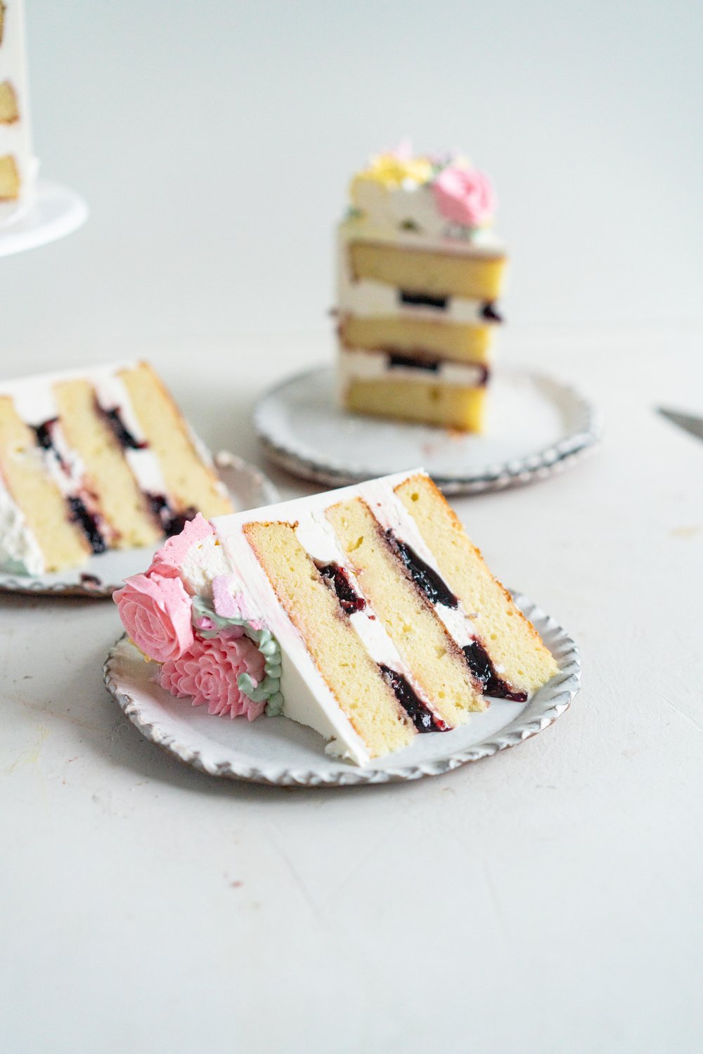 Lavender Blackberry Cake with Cream Cheese Frosting and a Piped Floral Wreath. Layers of delicately flavoured lavender cake are filled with a cream cheese frosting and blackberry jam, and topped with a beautiful floral wreath made from piped swiss meringue buttercream flowers. #pipedflowers #lavendercake #swissmeringuebuttercream #icingonthecakebook