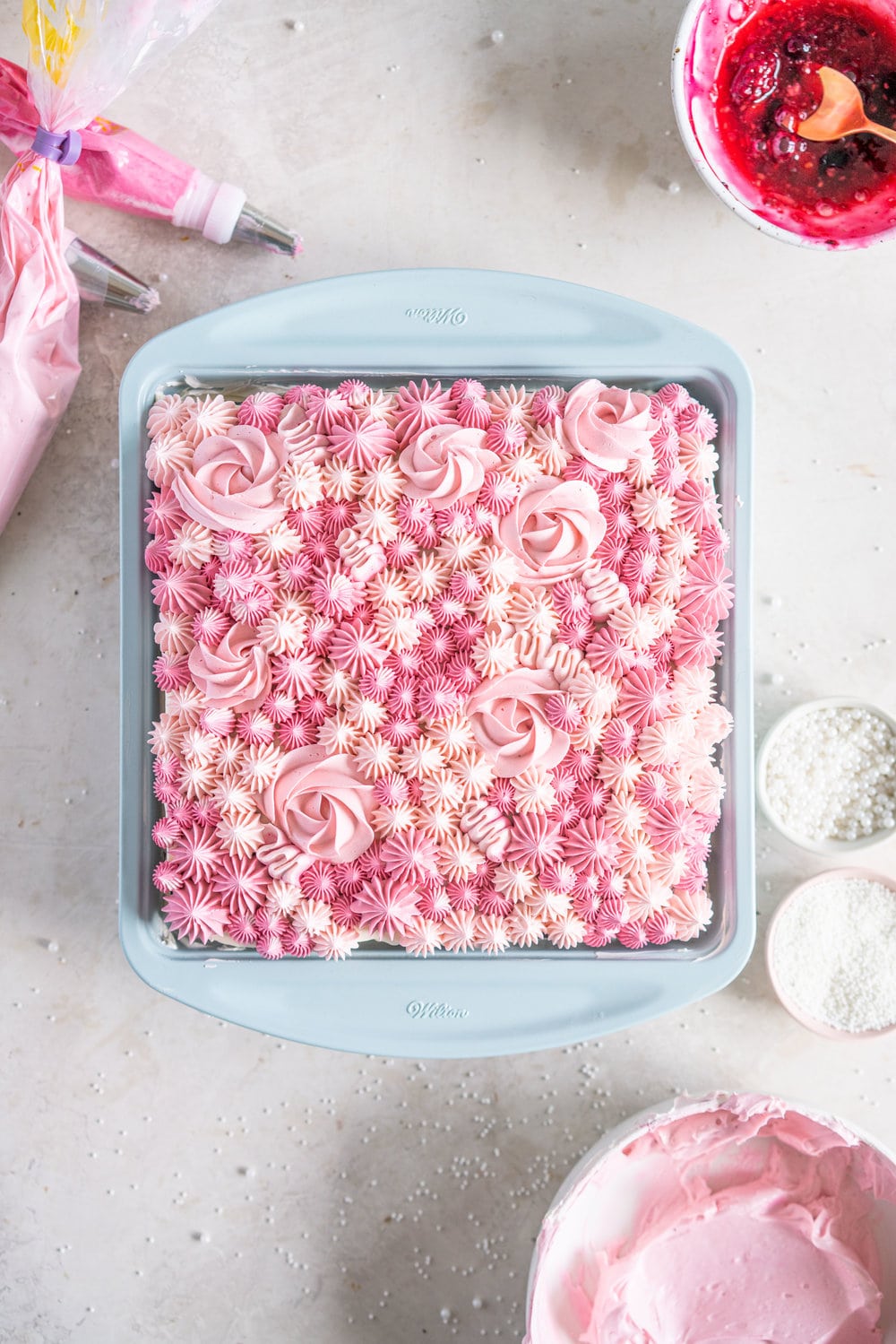 A super easy but delicious rich one bowl chocolate sheet cake is filled with a simple mixed berry cake filling and finished with a piped top using vanilla bean swiss meringue buttercream. This cake is baked in the new Wilton Texturra performance non-stick bakeware, and is finished with simple but beautiful piping in different shades of pink using various piping tips. This cake is simple yet elegant and is a perfect easy alternative to a layer cake. #chocolatecake #wilton #onebowlchocolatecake