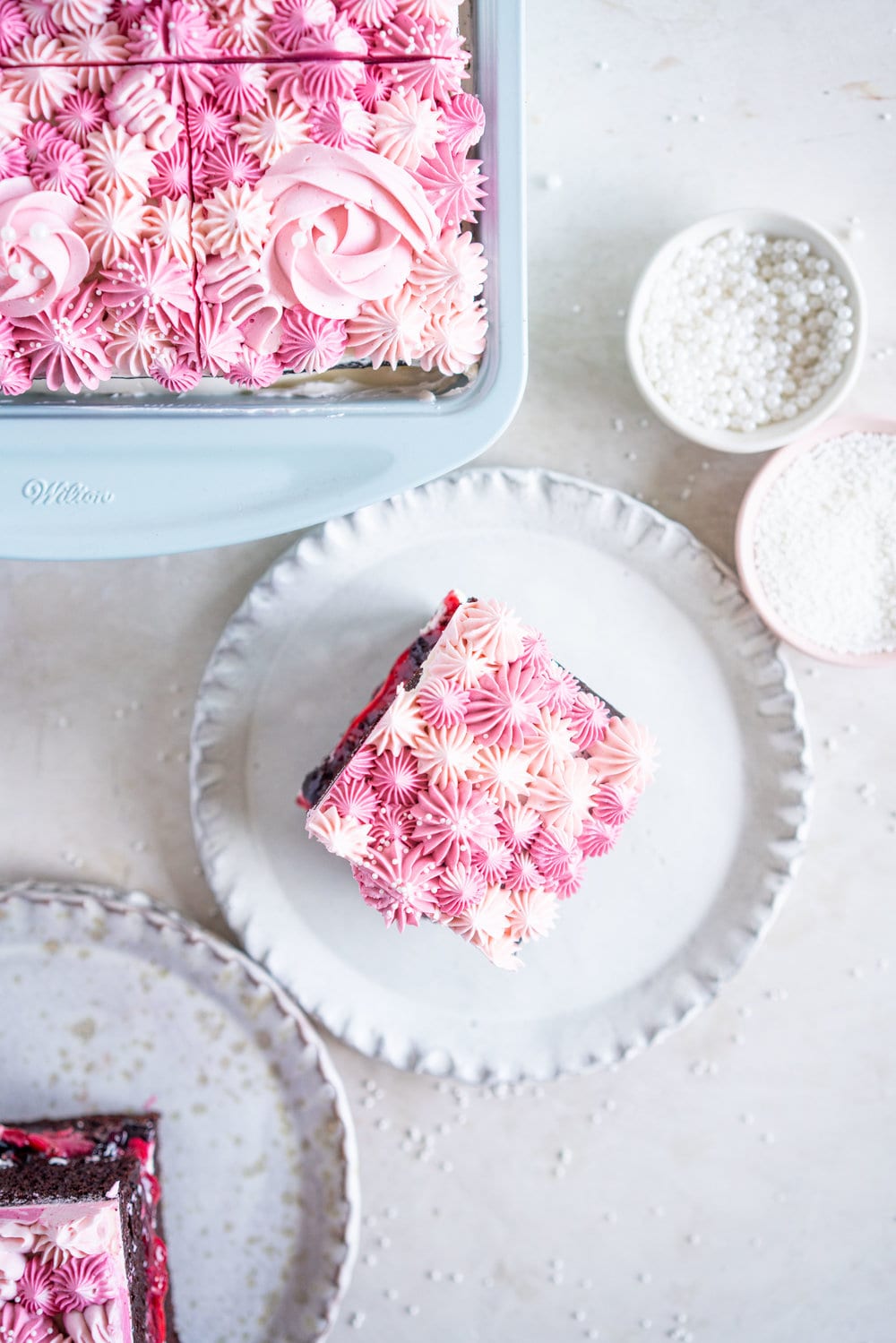 A super easy but delicious rich one bowl chocolate sheet cake is filled with a simple mixed berry cake filling and finished with a piped top using vanilla bean swiss meringue buttercream. This cake is baked in the new Wilton Texturra performance non-stick bakeware, and is finished with simple but beautiful piping in different shades of pink using various piping tips. This cake is simple yet elegant and is a perfect easy alternative to a layer cake. #chocolatecake #wilton #onebowlchocolatecake