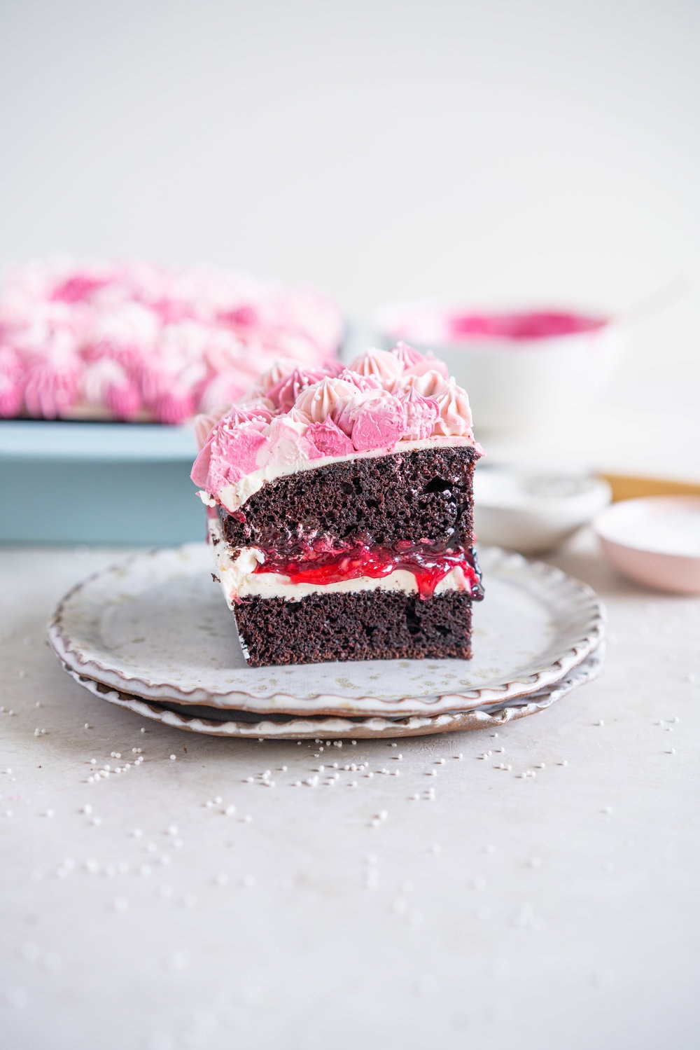 A super easy but delicious rich one bowl chocolate sheet cake is filled with a simple mixed berry cake filling and finished with a piped top using vanilla bean swiss meringue buttercream. This cake is baked in the new Wilton Texturra performance non-stick bakeware, and is finished with simple but beautiful piping in different shades of pink using various piping tips. This cake is simple yet elegant and is a perfect easy alternative to a layer cake. #chocolatecake #wilton #onebowlchocolatecake