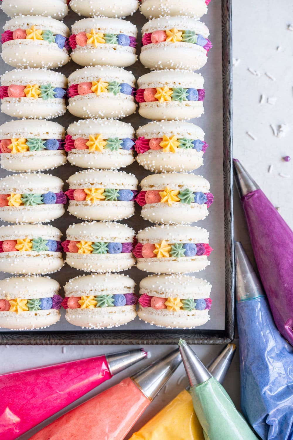 Rainbow macarons for pride - vanilla bean French macaron shells are filled with a vanilla bean swiss meringue buttercream, which is tinted the colours of the rainbow and piped around the shell. These are the perfect rainbow macaron for any occasion! #pride #Frenchmacarons #glutenfree #rainbowmacarons