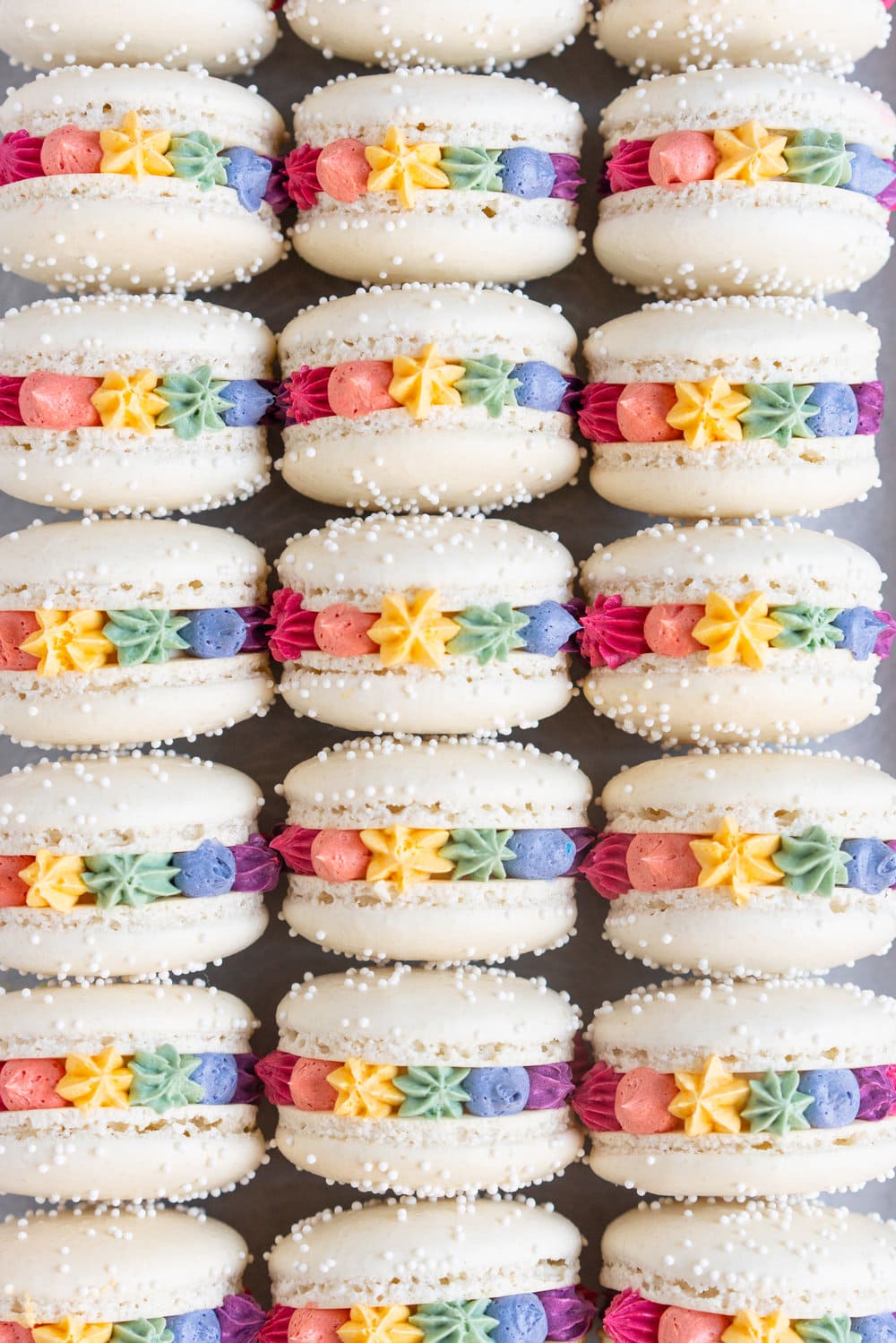 Rainbow macarons for pride - vanilla bean French macaron shells are filled with a vanilla bean swiss meringue buttercream, which is tinted the colours of the rainbow and piped around the shell. These are the perfect rainbow macaron for any occasion! #pride #Frenchmacarons #glutenfree #rainbowmacarons