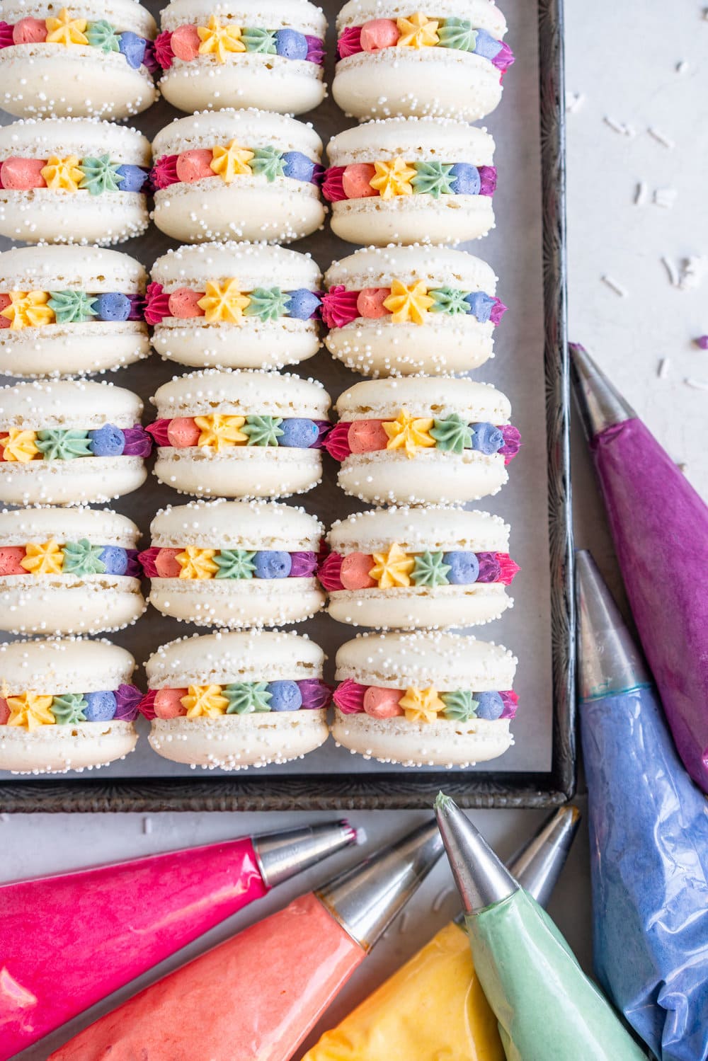 Rainbow macarons for pride - vanilla bean French macaron shells are filled with a vanilla bean swiss meringue buttercream, which is tinted the colours of the rainbow and piped around the shell. These are the perfect rainbow macaron for any occasion! #pride #Frenchmacarons #glutenfree #rainbowmacarons