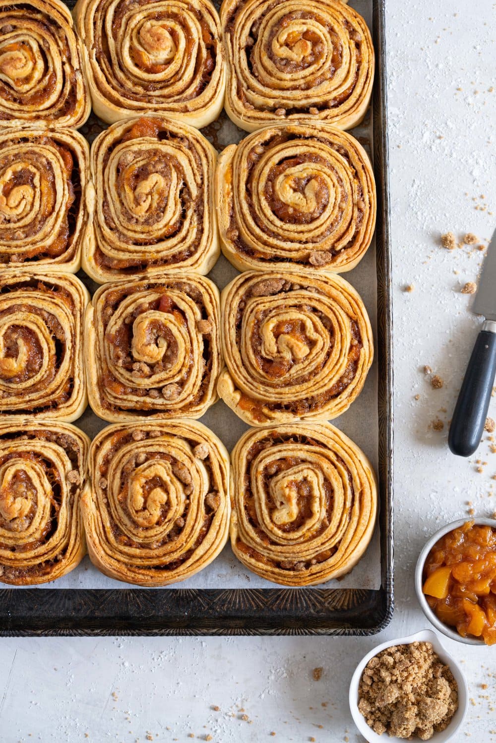 Laminated brioche cinnamon buns with peach compote and brown butter streusel. Soft and fluffy brioche is layered with cinnamon sugar, then filled with a brown butter streusel and peach compote, and finished with a powdered sugar glaze. These are the perfect summer treat. #briochebuns #cinnamonbuns #laminatedbriochebuns #peachcompote