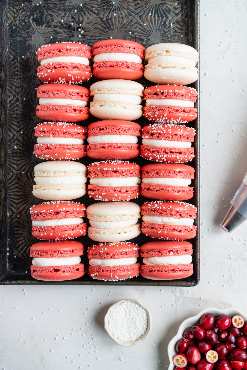 Cranberry and white chocolate macarons. French macaron shells are filled with white chocolate swiss meringue buttercream and fresh cranberry sauce filling, for the perfect festive macaron. These gluten free treats are easy to make for a crowd.