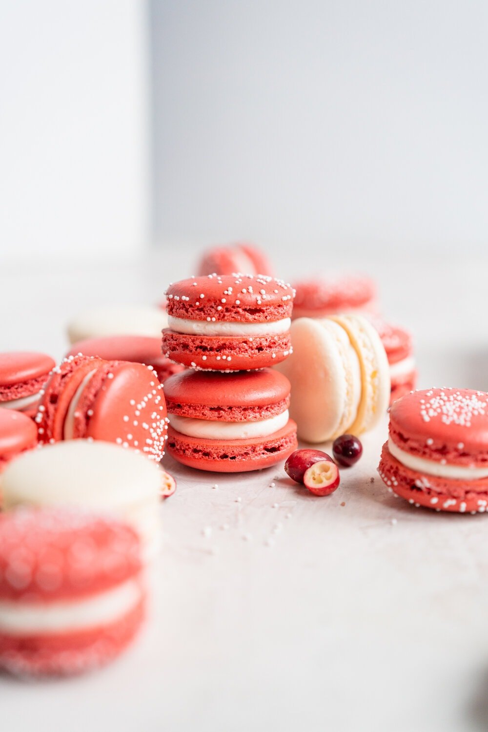 Cranberry and white chocolate macarons. French macaron shells are filled with white chocolate swiss meringue buttercream and fresh cranberry sauce filling, for the perfect festive macaron. These gluten free treats are easy to make for a crowd.