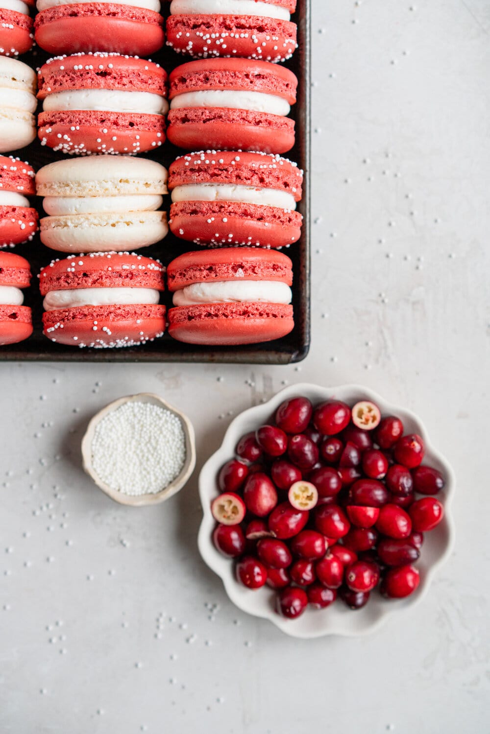 Cranberry and white chocolate macarons. French macaron shells are filled with white chocolate swiss meringue buttercream and fresh cranberry sauce filling, for the perfect festive macaron. These gluten free treats are easy to make for a crowd.