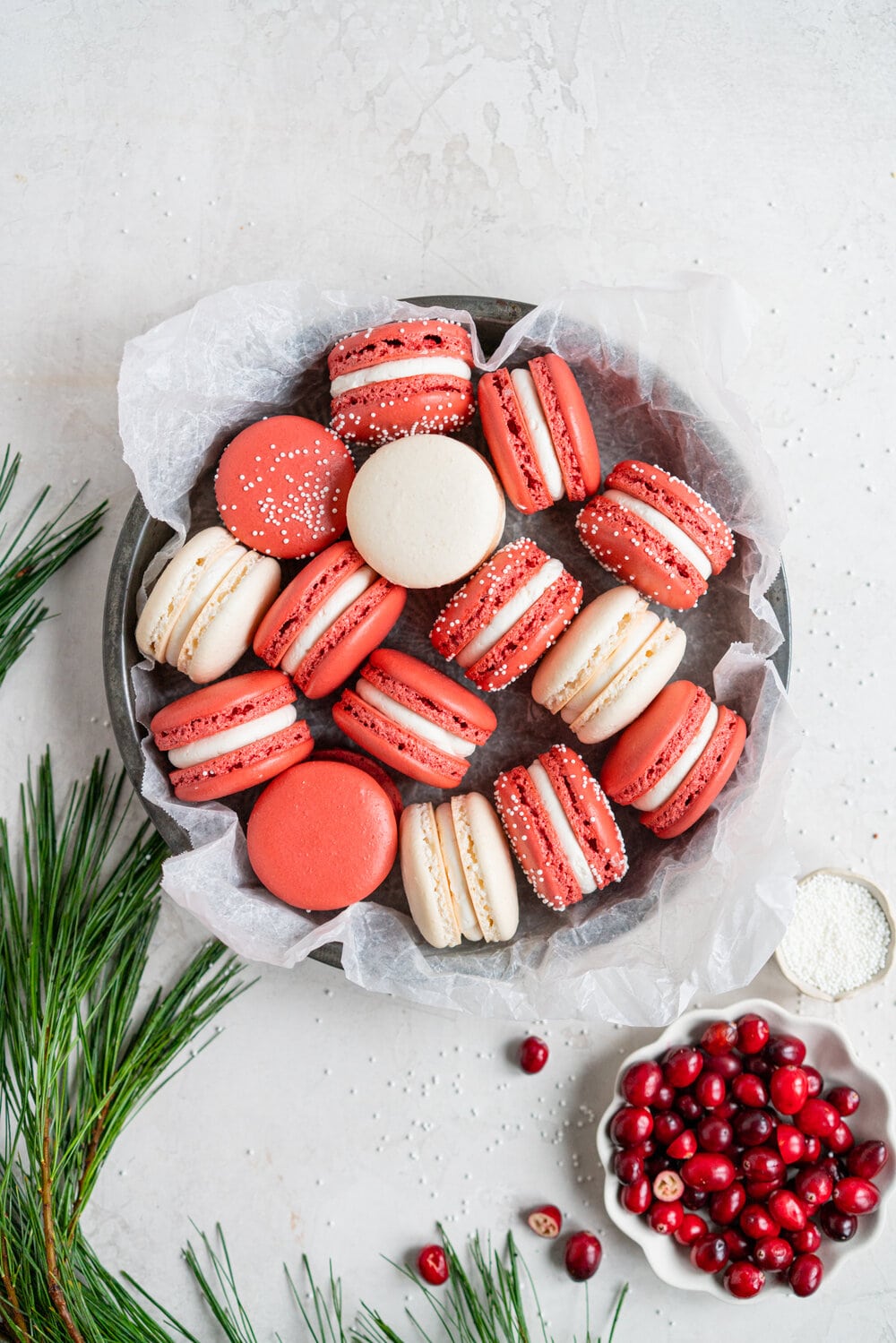 Cranberry and white chocolate macarons. French macaron shells are filled with white chocolate swiss meringue buttercream and fresh cranberry sauce filling, for the perfect festive macaron. These gluten free treats are easy to make for a crowd.