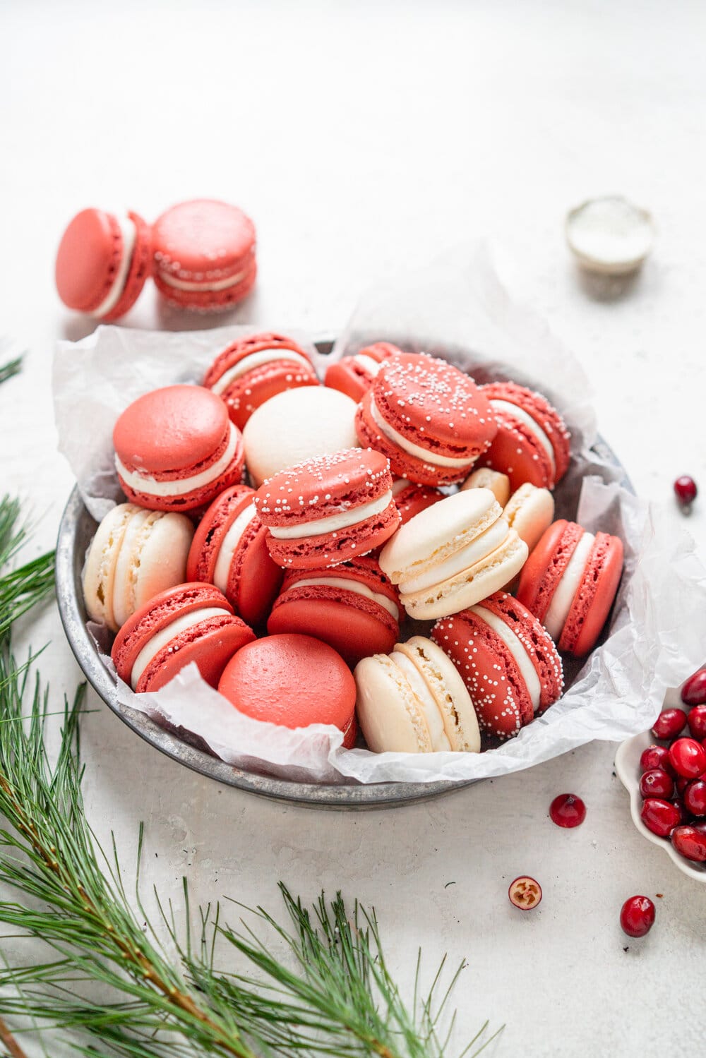 Cranberry and white chocolate macarons. French macaron shells are filled with white chocolate swiss meringue buttercream and fresh cranberry sauce filling, for the perfect festive macaron. These gluten free treats are easy to make for a crowd.