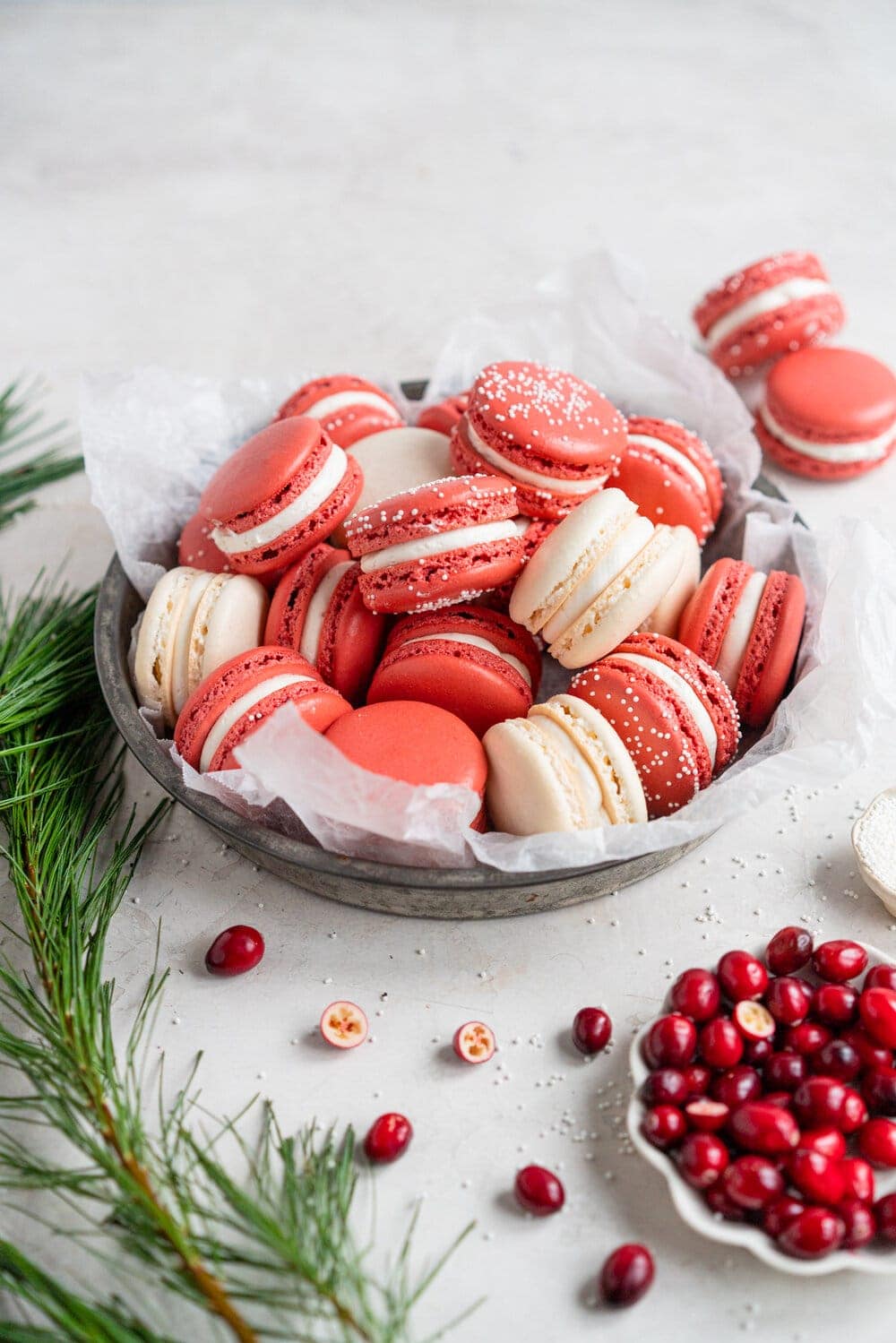 Cranberry and white chocolate macarons. French macaron shells are filled with white chocolate swiss meringue buttercream and fresh cranberry sauce filling, for the perfect festive macaron. These gluten free treats are easy to make for a crowd.