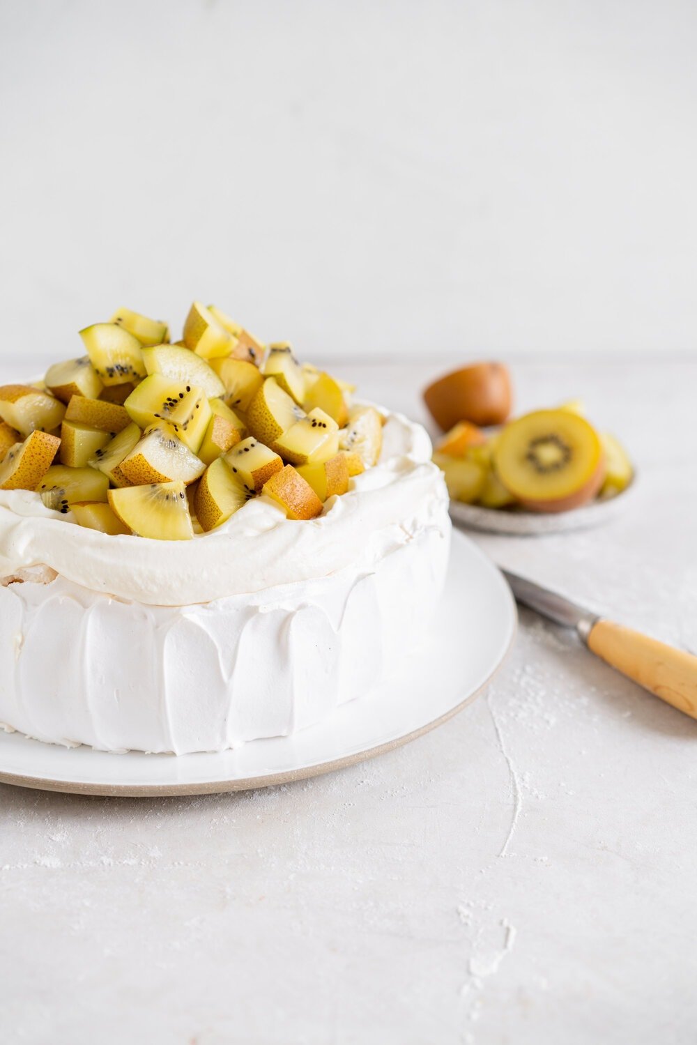 The most perfect, easy pavlova recipe. Using Swiss Meringue instead of the traditional French, this pavlova recipe is crispy on the outside and has a perfect, full, marshmallow center, and is much more stable so is resistant to humidity and changes in weather. It is easy to make and the perfect crowd pleaser. This is the most perfect year round dessert. Topped with Manuka Honey whipped cream and golden kiwifruit, this is a New Zealand classic.