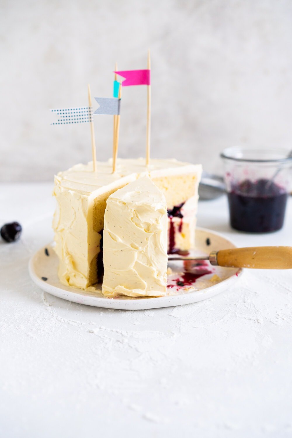 Two Layer Vanilla Bean Buttermilk Cake with Cherry Compote and Vanilla Bean Swiss Meringue Buttercream with a slice taken out.