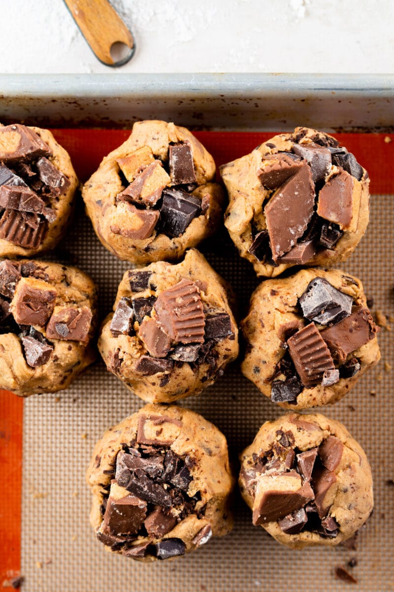Balls of cookie dough with peanut butter cups and chocolate chunks on top.