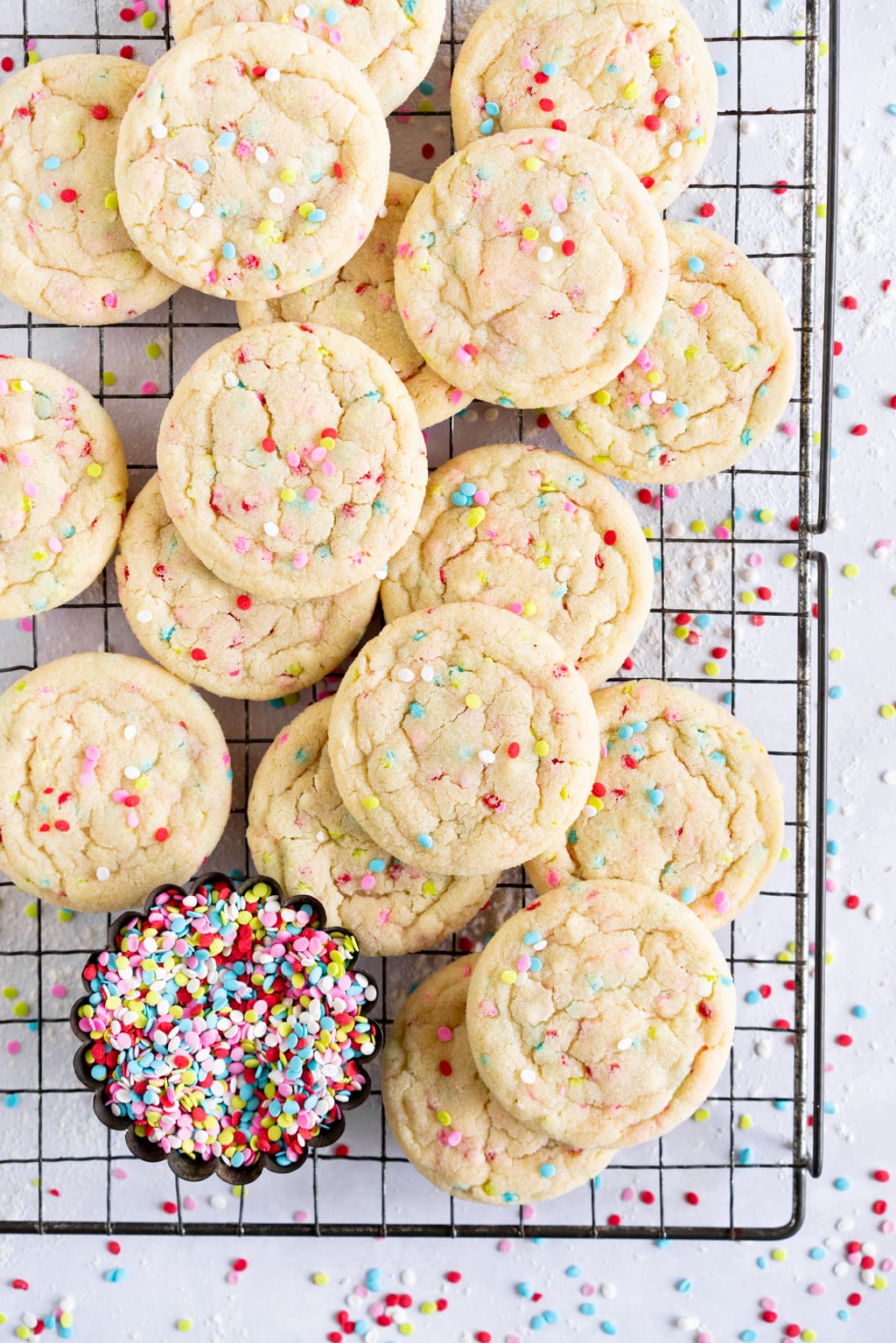 stacked up funfetti sugar cookies on wire rack with sprinkles in background