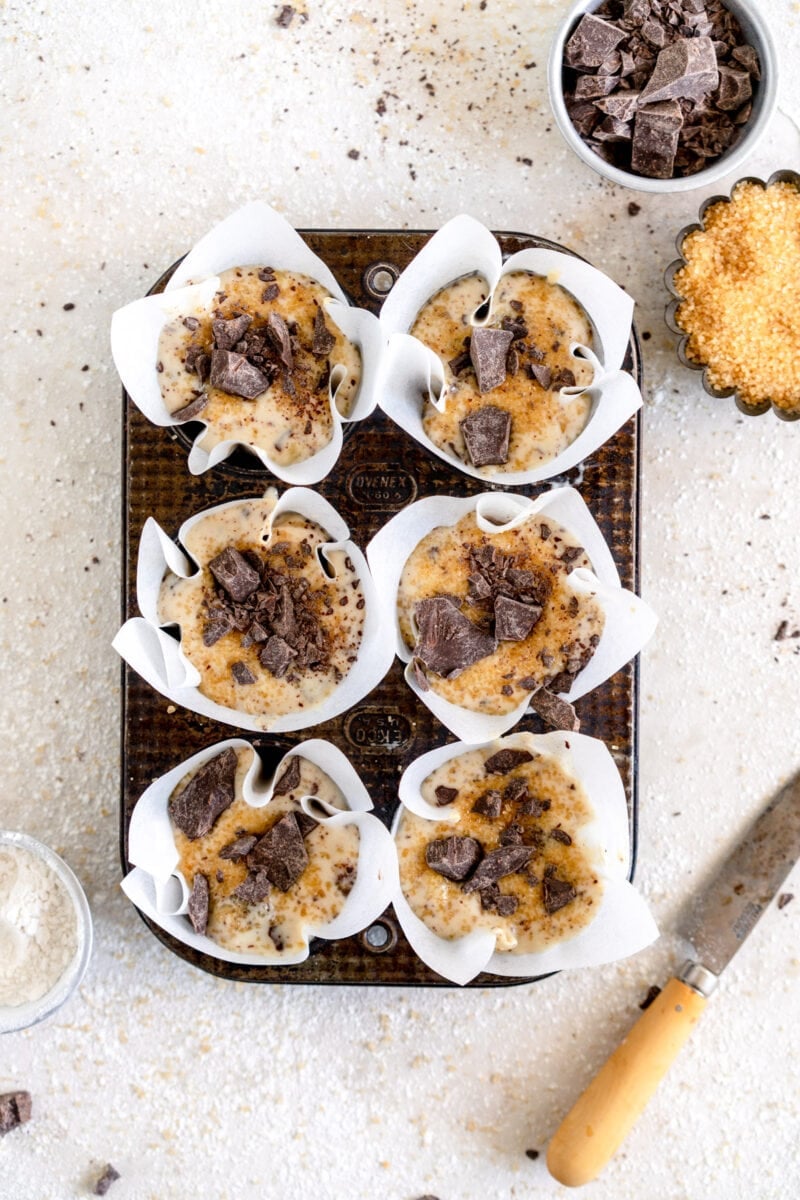 muffin batter in muffin pan with chocolate and sugar
